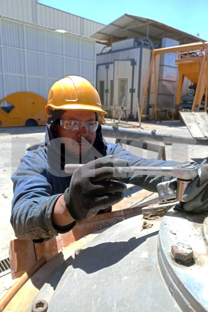 hombre con casco amarillo realizando mantenimiento a una planta mezcladora de concreto